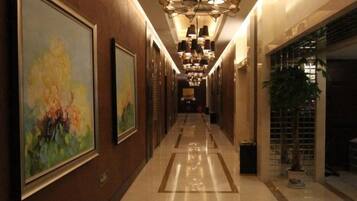 A hotel corridor with framed artwork on the walls, a chandelier, and a potted plant.