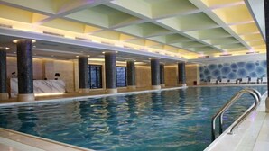 An indoor swimming pool with a tiled floor, a metal handrail, and a ceiling with a geometric pattern.