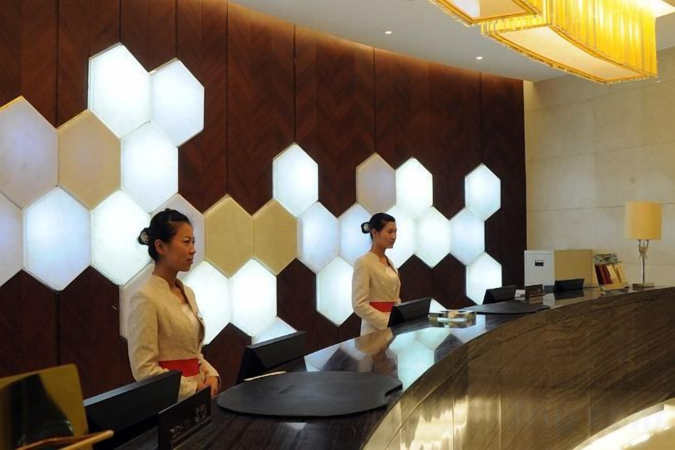 A reception desk with a modern design, featuring a geometric light pattern on the wall and a sleek, dark counter.