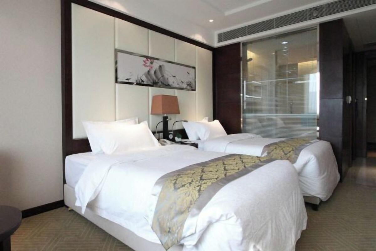 Habitación de hotel con dos camas, un ventanal grande, un cuadro en la pared y una lámpara.
