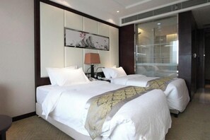 Habitación de hotel con dos camas, un ventanal grande, un cuadro en la pared y una lámpara.