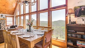 Uma sala de jantar com mesa de madeira posta para quatro, janelas amplas e um lustre.