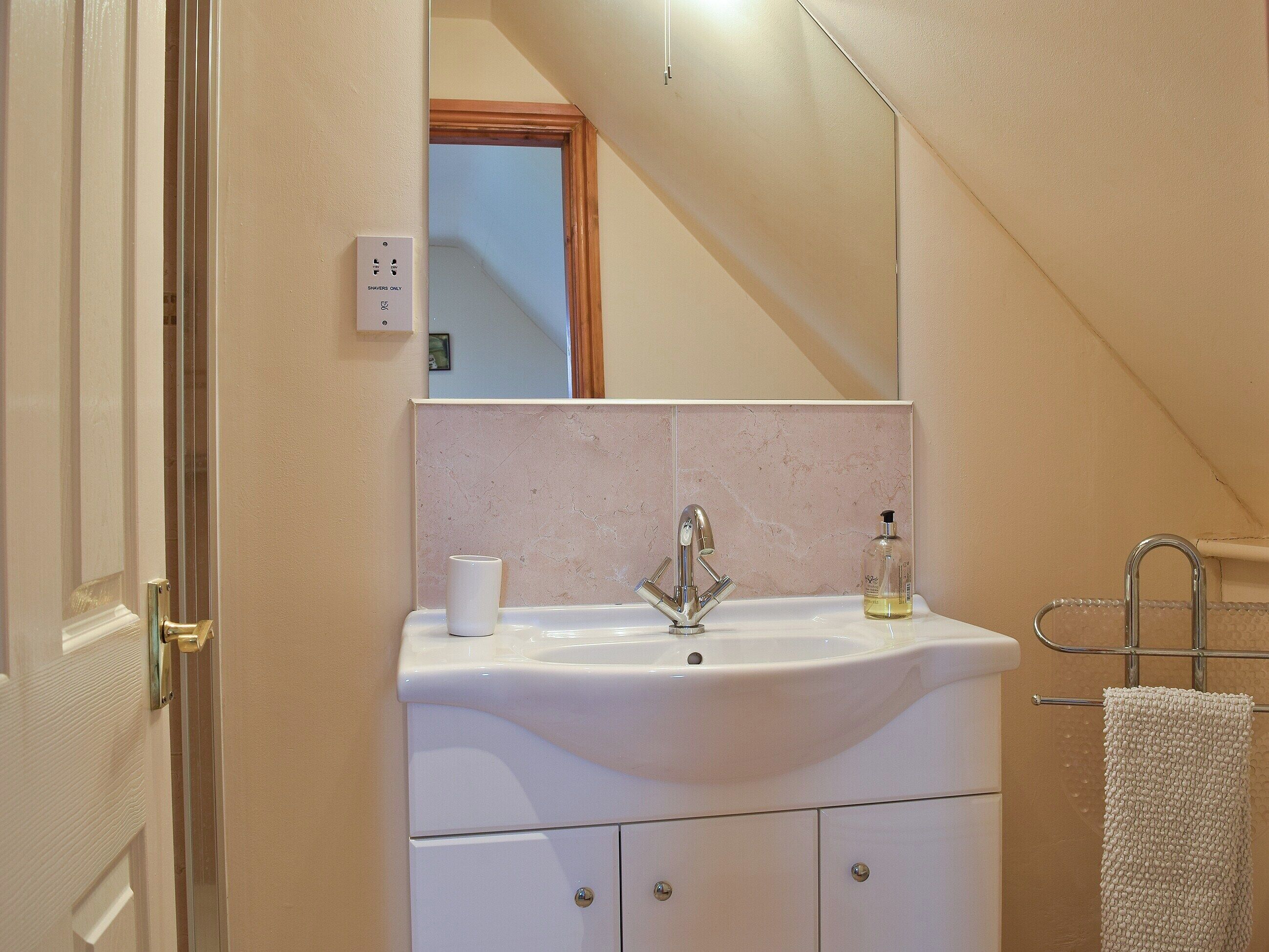 Een badkamer met een wastafel, spiegel, handdoekhouder en een deur naar een andere kamer.