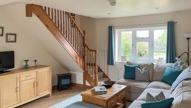 Ein Wohnzimmer mit einer Holztreppe, einer Sofagarnitur, einem kleinen Tisch und einem Fernseher auf einer Holzkommode.