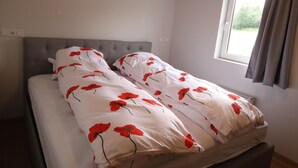 A bed with a grey headboard and white bedding with red floral patterns. - Selfell Guesthouse - Apartment 1 (Kirkjubæjarklaustur)