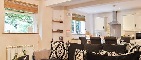 A living room with a sofa, a dining area with chairs, a kitchen with cabinets, and a window with blinds.