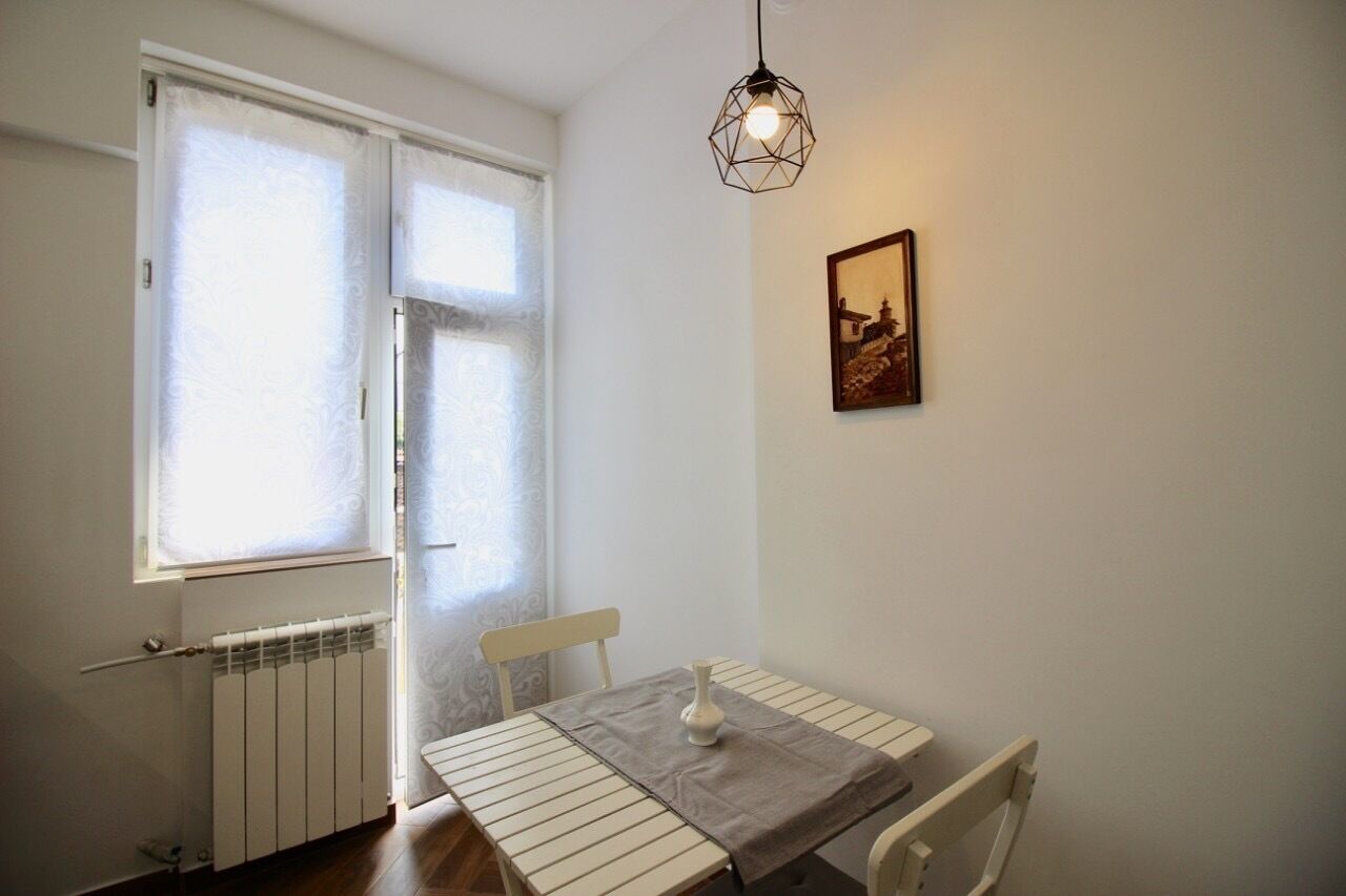 A room with a table, chairs, a radiator, a window with frosted glass, and a hanging light fixture.