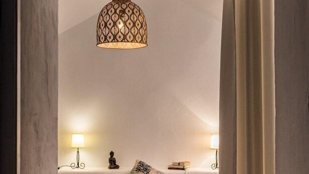 A bedroom with a bed, two bedside lamps, a decorative hanging light, and a small Buddha statue. - Hotel Rancho Los Lobos (Jimena de la Frontera)