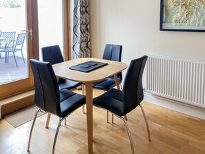 Un espace repas moderne avec une table ronde en bois, des chaises à revêtement noir et une vue sur l’extérieur grâce à une porte vitrée.