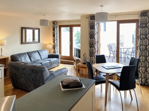 A modern living room with a grey sofa, a dining table with chairs, and a small kitchen area.
