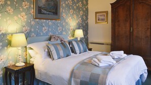 Una habitación de hotel con papel tapiz floral, una cama con almohadones a rayas, dos lámparas de noche y un armario de madera.