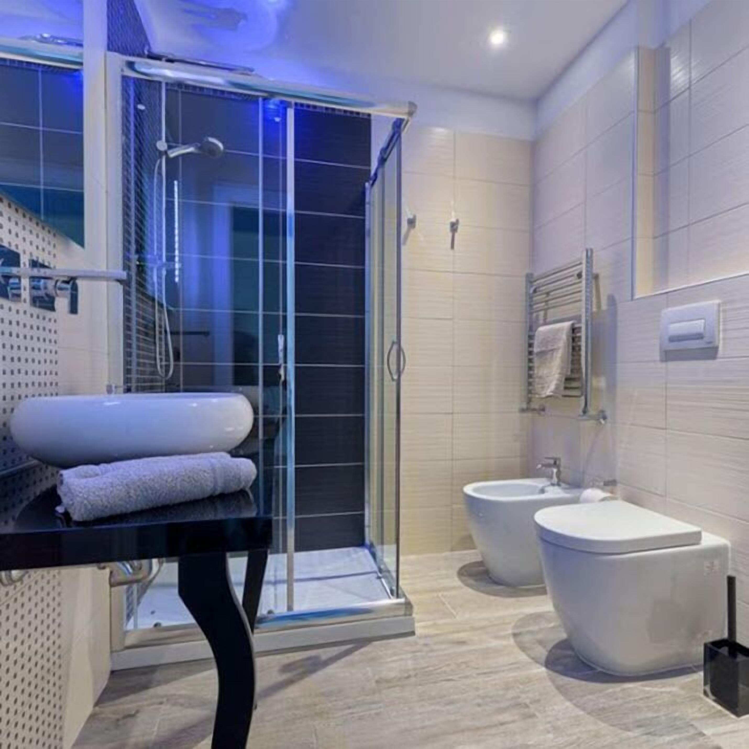 A modern bathroom with a glass shower enclosure, a bidet, a toilet, and a sink with towels.