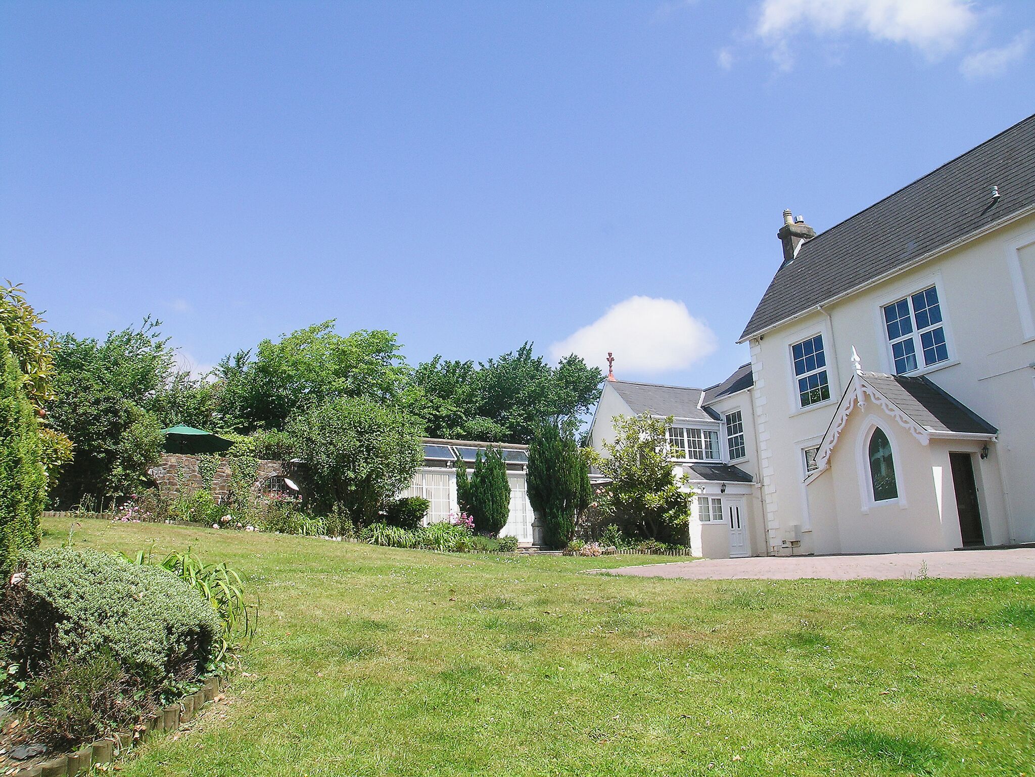 A large white building with multiple windows and a grey roof, surrounded by a well-maintained lawn and trees.