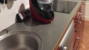 Een keuken met een roestvrijstalen spoelbak, een rode en zwarte keukenmachine en een zwart inductiekookplaat.