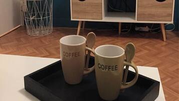 Moderni olohuone, jossa on valkoinen sohva, musta tarjotinpöytä, jossa on kaksi kahvikuppia, televisio ja sininen seinä.