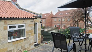 A patio area with a table and chairs, a potted plant, and a view of a brick house with a tiled roof.