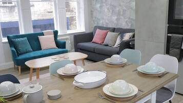 A dining area with a wooden table set for four, surrounded by a teal sofa and a grey sofa with cushions.