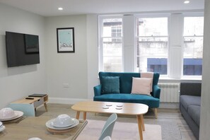 Un salon avec un canapé de couleur turquoise, une table basse en bois et un coin repas avec une table dressée pour deux personnes.