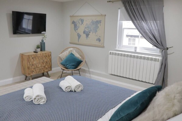 Une chambre d’hôtel avec un lit, une armoire en bois, une chaise, une carte accrochée au mur, une fenêtre avec des rideaux et un téléviseur.
