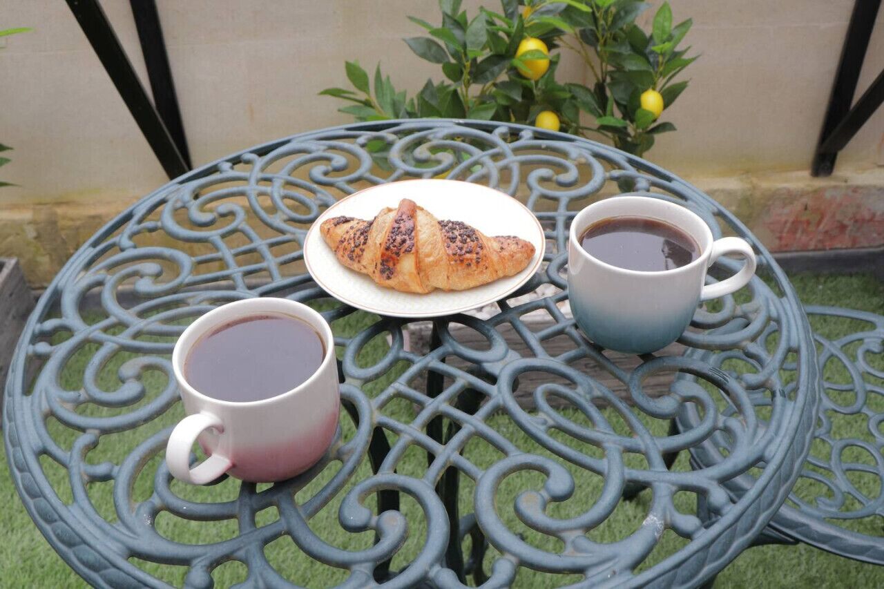 A round metal table with a plate of croissant and two cups of coffee.