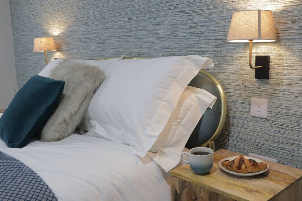 A hotel room with a bed, a nightstand with a lamp, a cup, and a plate of food.