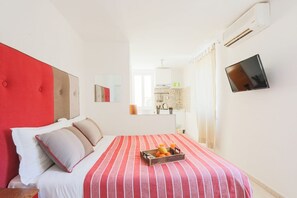 Hotellihuone, jossa on sänky, seinälle asennettu televisio ja ikkuna, jossa on verhot.