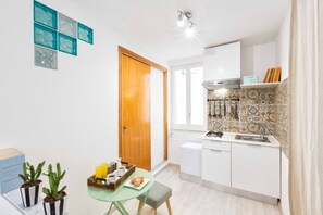 Kompakti keittiö, jossa on pieni ruokailutila, puuovi ja laatoitettu seinäosa työtason yläpuolella.