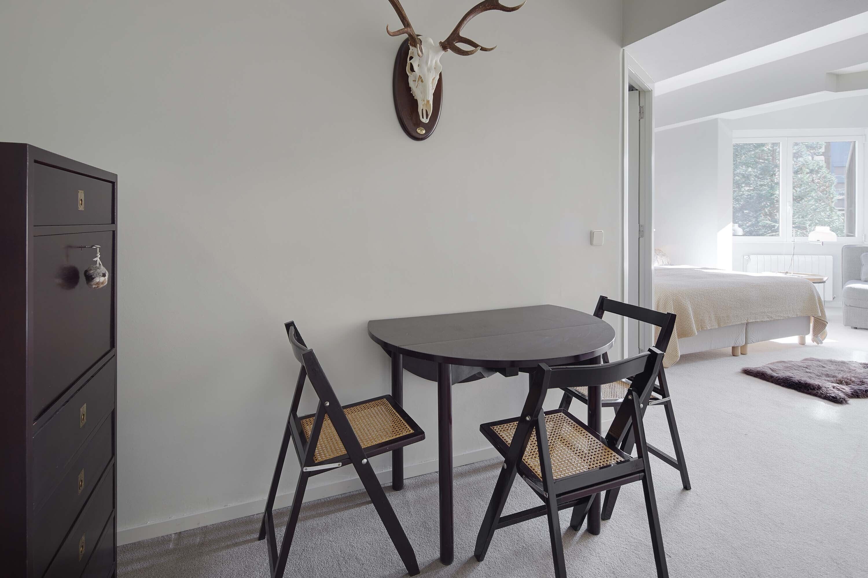 A room with a bed, a desk, and a chair. There is a wall-mounted deer skull decoration.
