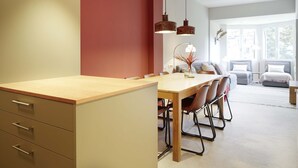 Un espace de salle à manger moderne avec une table et des chaises en bois, un mur d’accent rouge et des luminaires suspendus.
