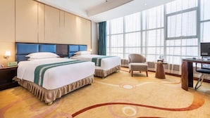 Une chambre d’hôtel avec deux lits, un bureau, une chaise et de grandes fenêtres.