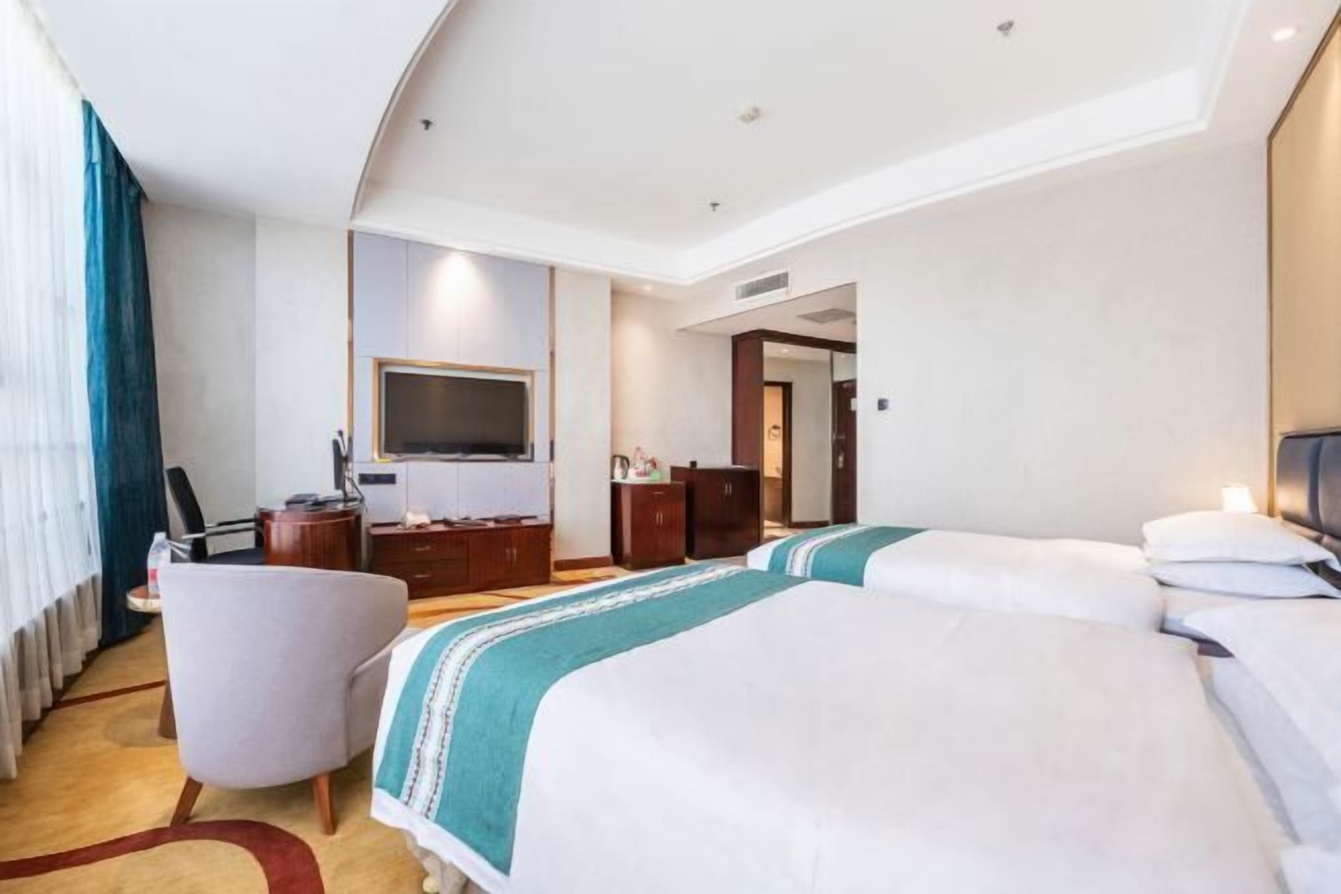 A hotel room with a large bed, a desk, a chair, a TV, and a wardrobe.