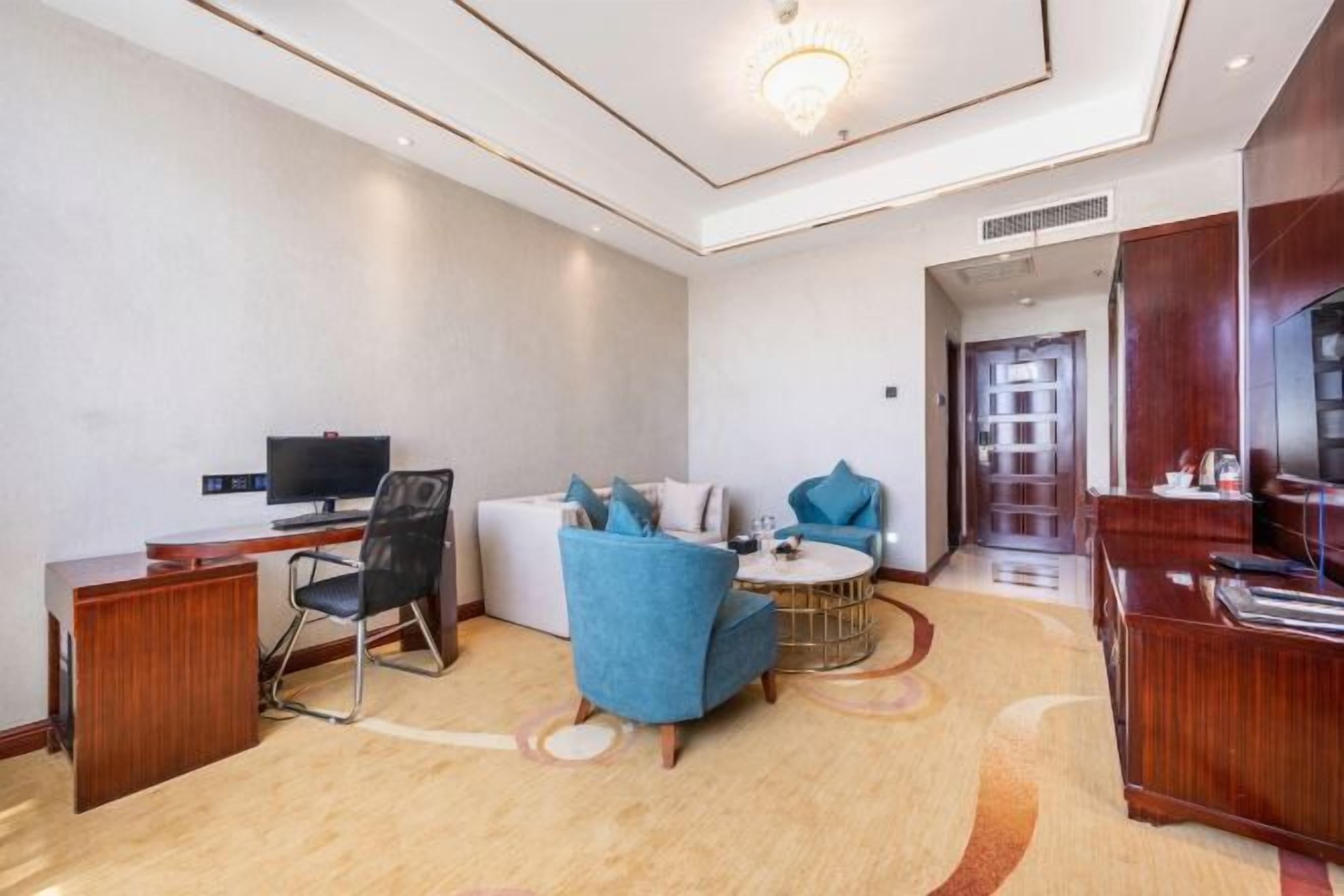 Una habitación de hotel moderna con un escritorio, un sillón azul, un sofá y un televisor.