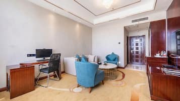 Una habitación de hotel moderna con un escritorio, un sillón azul, un sofá y un televisor.