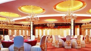 Une salle de banquet avec des tables rondes, des chaises blanches ornées de nœuds, des lustres et une moquette rouge.