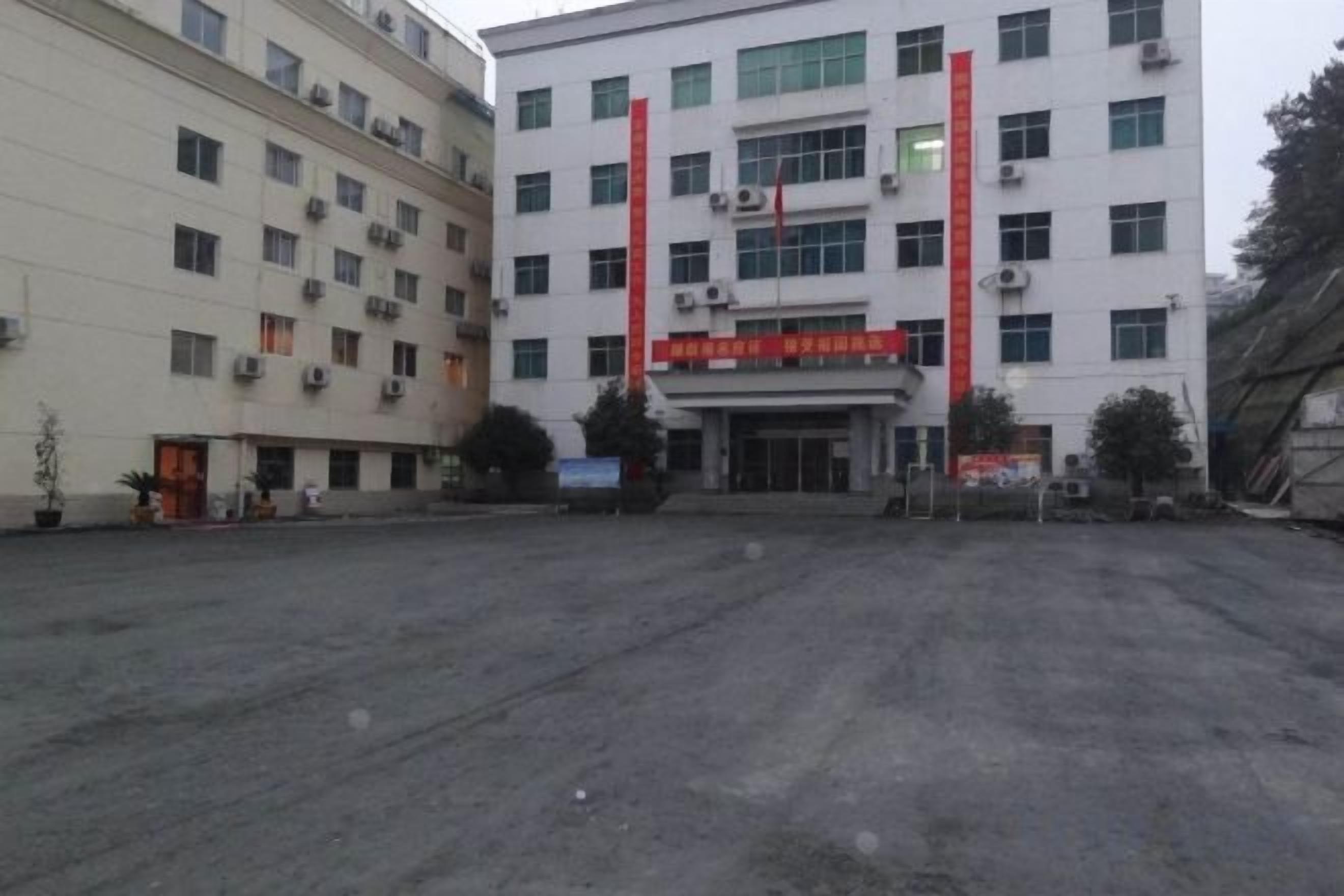 A building with multiple floors, a red banner, and a paved ground in front.
