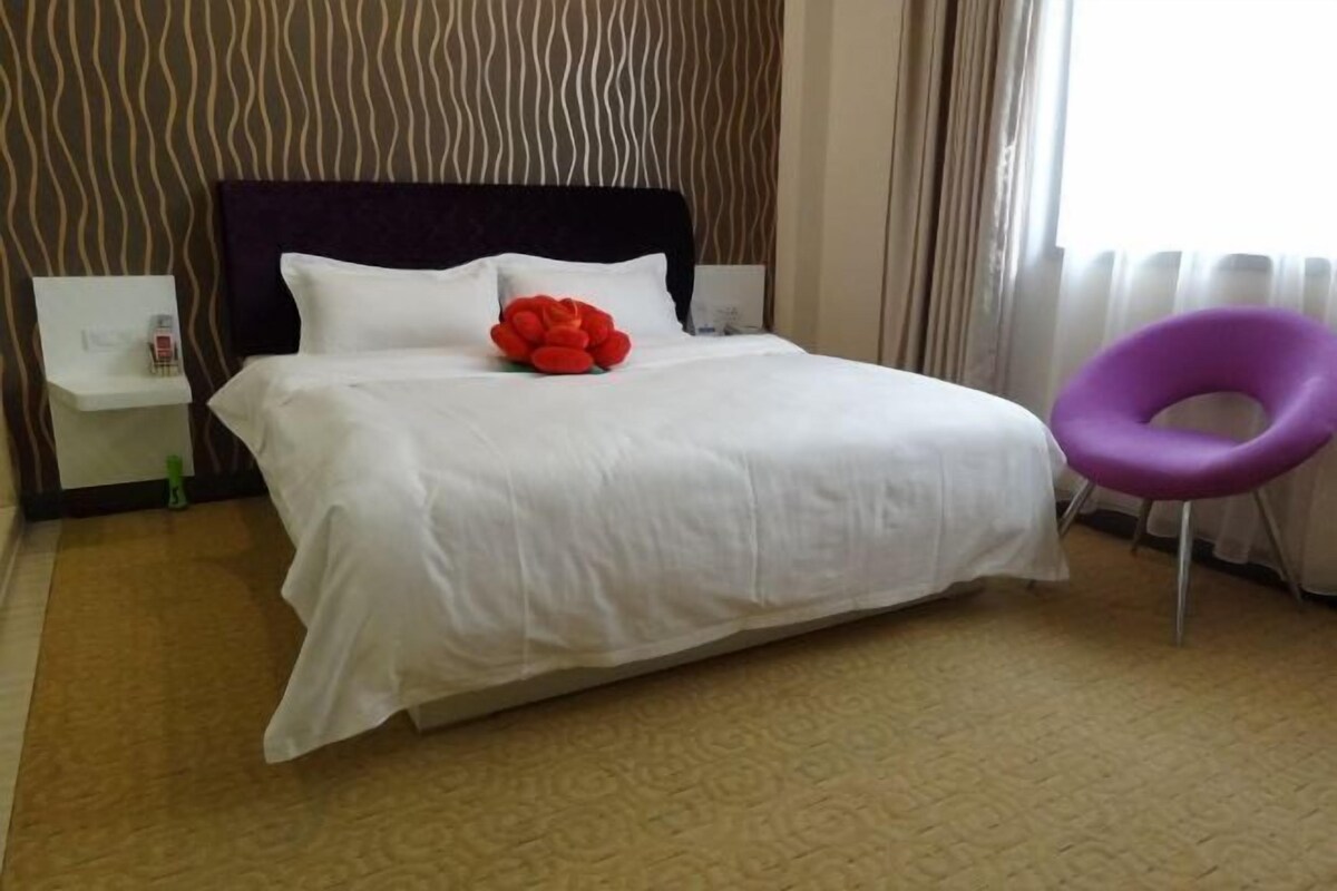 A hotel room with a large bed, a nightstand, a purple chair, and a patterned wall.