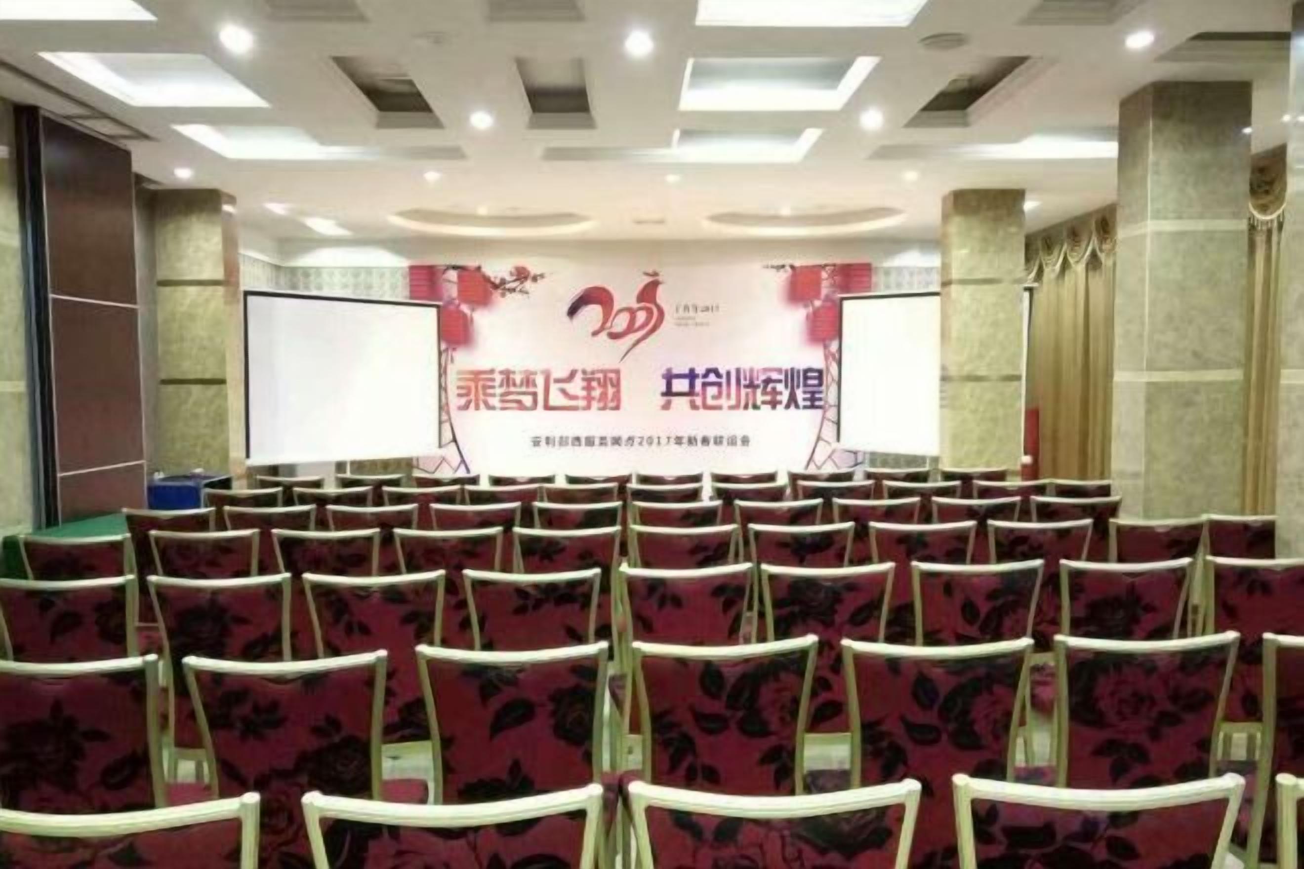 A conference room with rows of chairs, a large screen, and a banner with text.