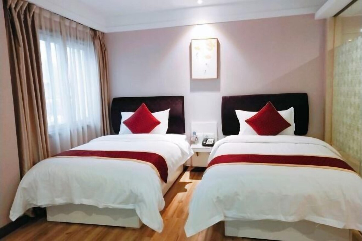 A hotel room with two beds, each with white bedding and red accents, a bedside table with a phone, and a window with curtains.