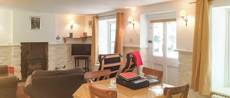 Un comedor con una mesa dispuesta para cuatro personas, una chimenea y un televisor al fondo.
