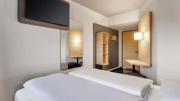 Una habitación de hotel con una cama, un televisor de pantalla plana, un espejo y una estantería de madera.