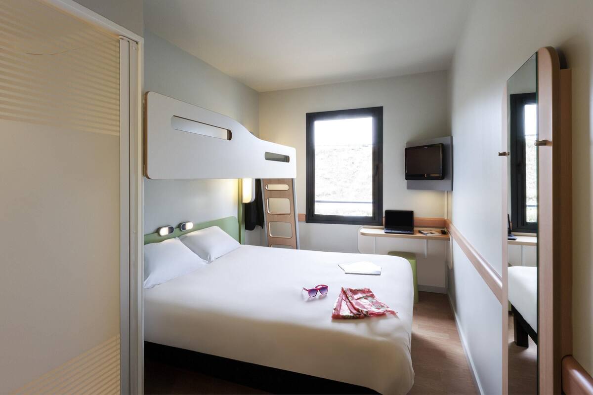 A hotel room with a bed, a desk, a television, and a window.