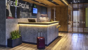 A reception desk with a monitor, a red suitcase, and a plant. - Ibis Budget Valencia Alcasser (Silla)