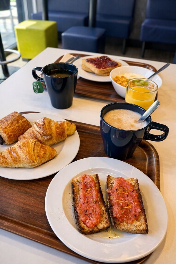 A breakfast tray with croissants, toast with tomato, a mug of coffee, a bowl of cereal, and a glass of orange juice. - Ibis Budget Valencia Alcasser (Silla)