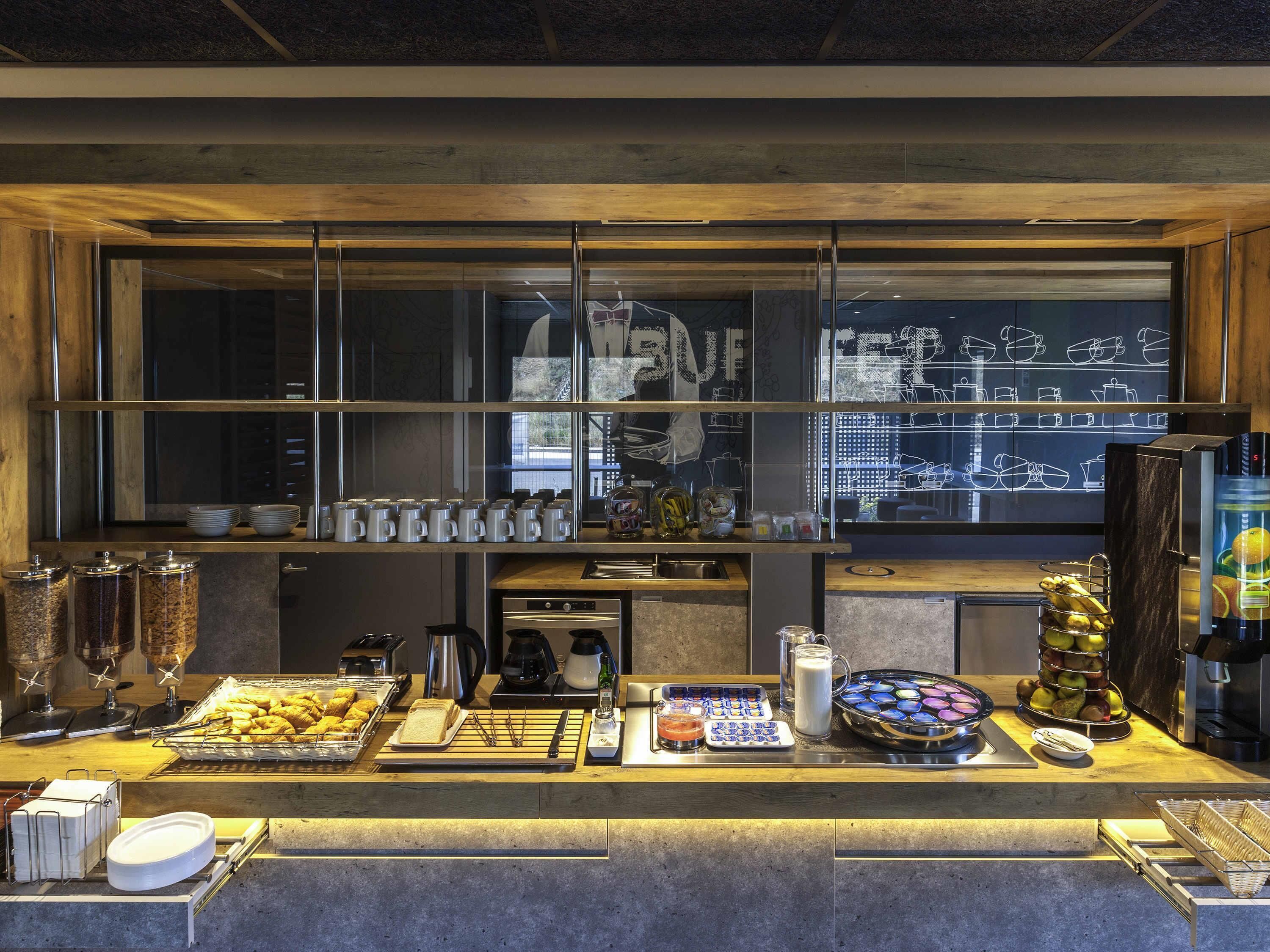 Mostrador de buffet con diversos alimentos, una máquina de café y un refrigerador.