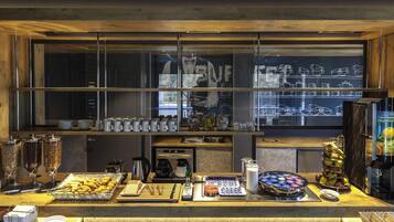 Mostrador de buffet con diversos alimentos, una máquina de café y un refrigerador.