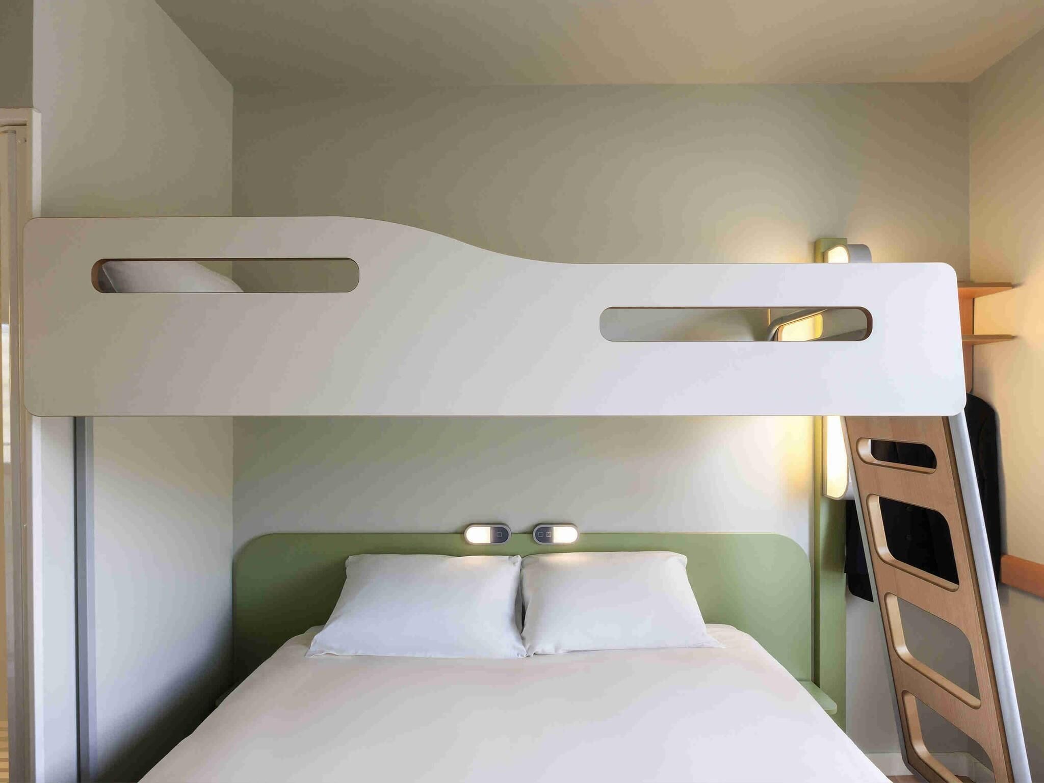 Una cama individual con escalera, una mesita de noche con lámpara y un cabecero verde.