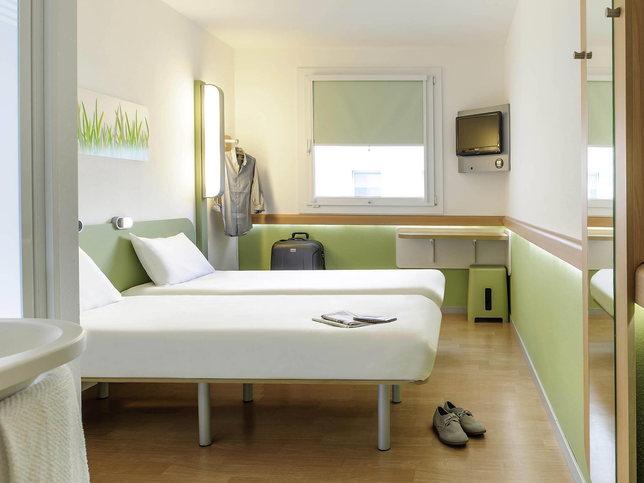 A hotel room with two beds, a desk, a TV, and a suitcase.