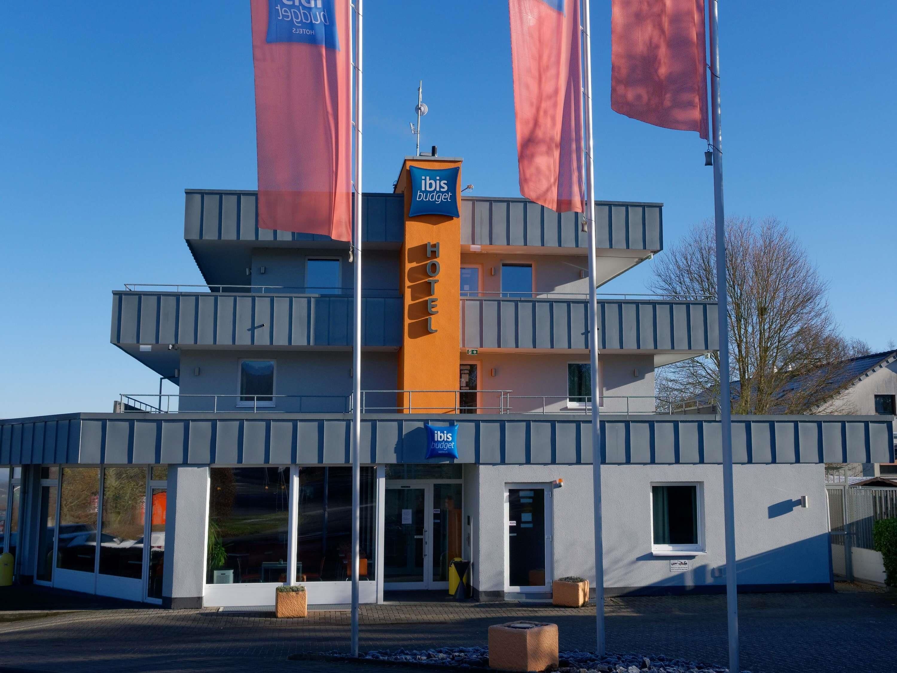 Ein modernes Hotel mit einer markanten Fassade in Orange und Grau, mehreren Balkonen und blauem Himmel.
