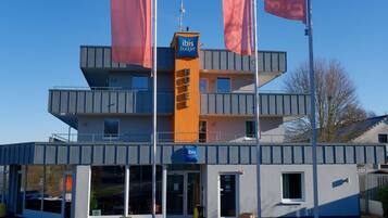 Ein modernes Hotel mit einer markanten Fassade in Orange und Grau, mehreren Balkonen und blauem Himmel.