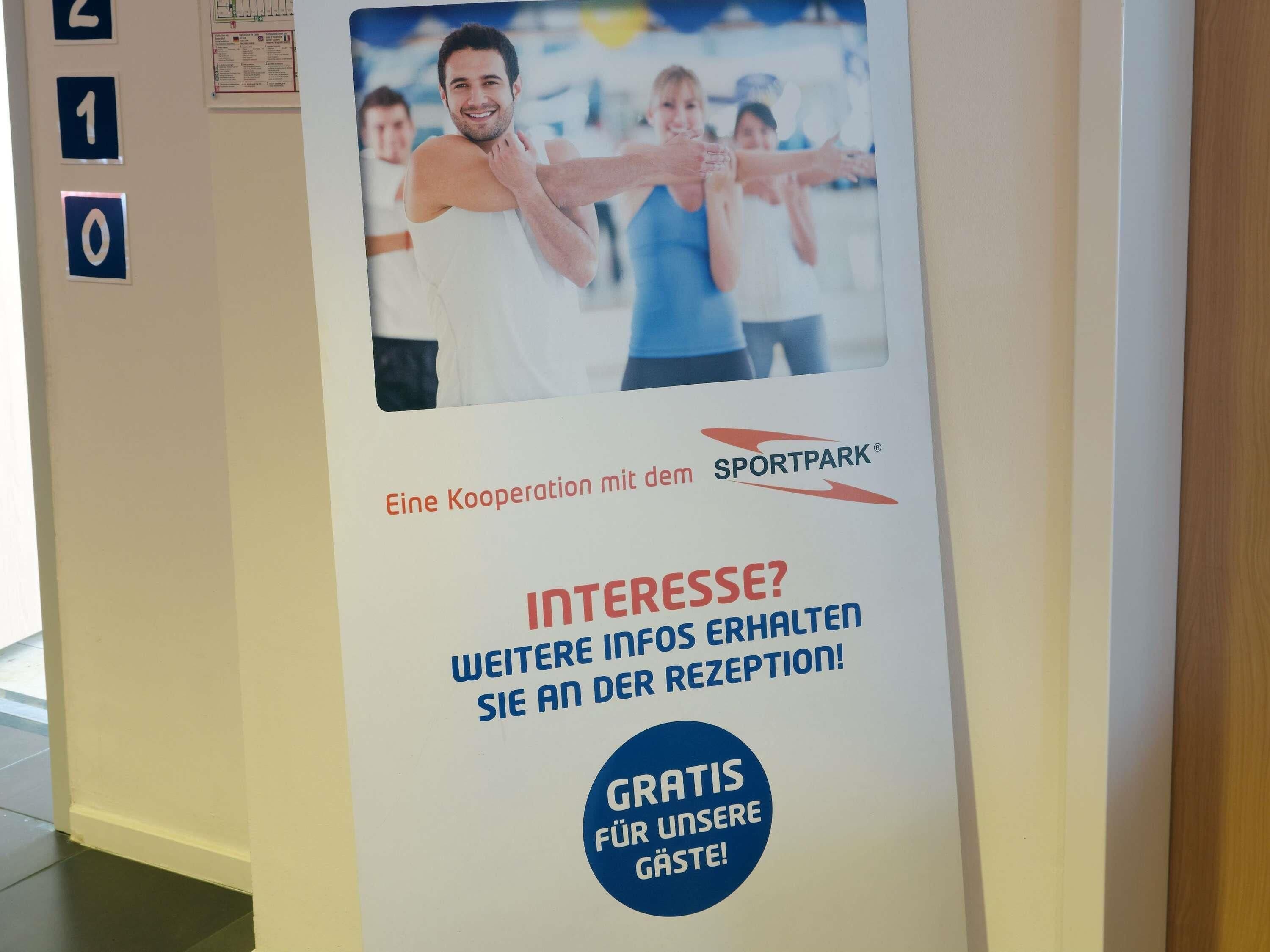 Un cartel con una foto de personas ejercitándose, colaboración con Sportpark y una oferta informativa gratuita en recepción.